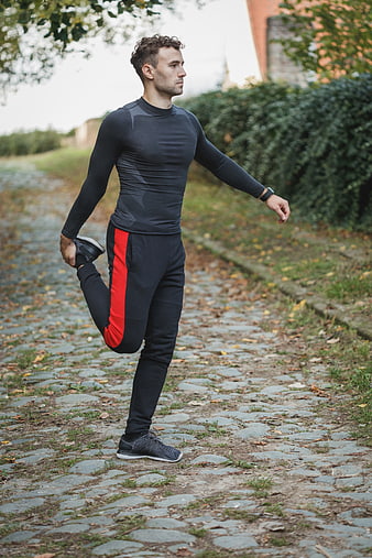 Athletic Man Stretching Leg on Cobblestone Path