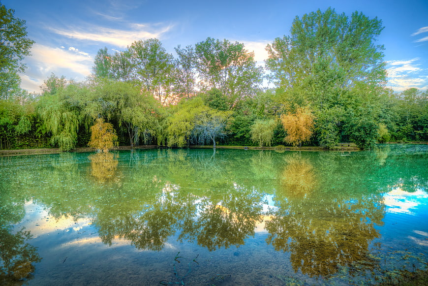 Serene lake with vibrant green trees and clear blue sky reflection