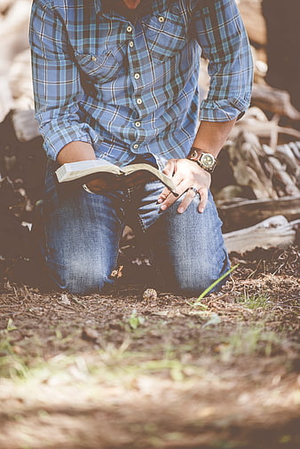 Man kneeling in forest reading book outdoors