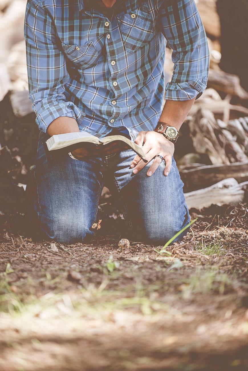 Man kneeling in forest reading book outdoors