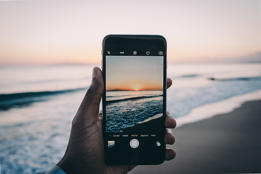 Hand holding smartphone capturing sunset ocean beach photo