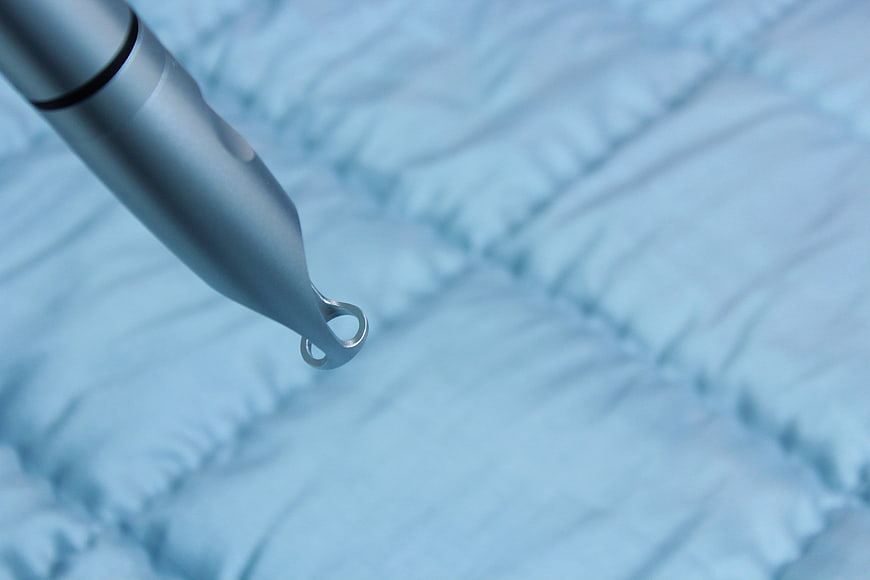 Close-up of a silver medical laser device tip on a blue textured surface