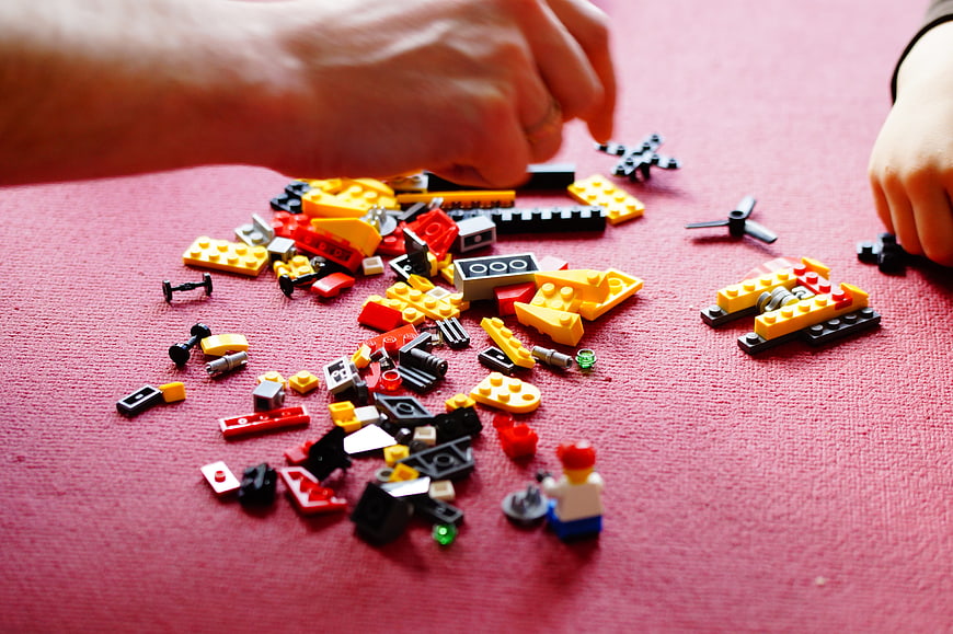 Father and child building with colorful Lego blocks on red surface