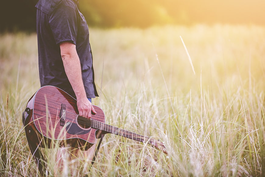 Man holding acoustic guitar in sunlit grassy field