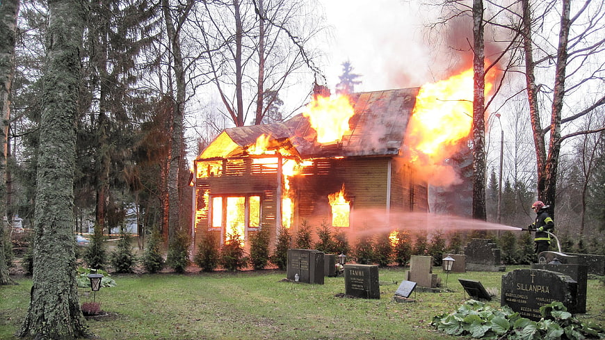 Firefighter extinguishing burning wooden house in cemetery