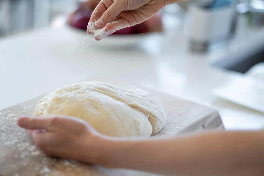 Hands sprinkling flour on dough in a bright kitchen
