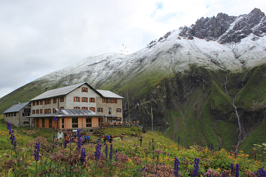Alpine mountain hut with wildflowers and snow-capped peaks