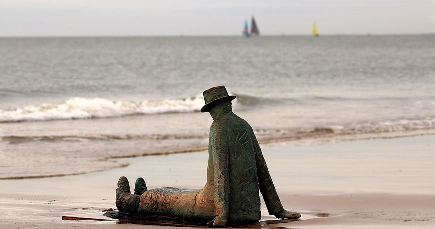 Bronze statue of man sitting on beach looking at sea