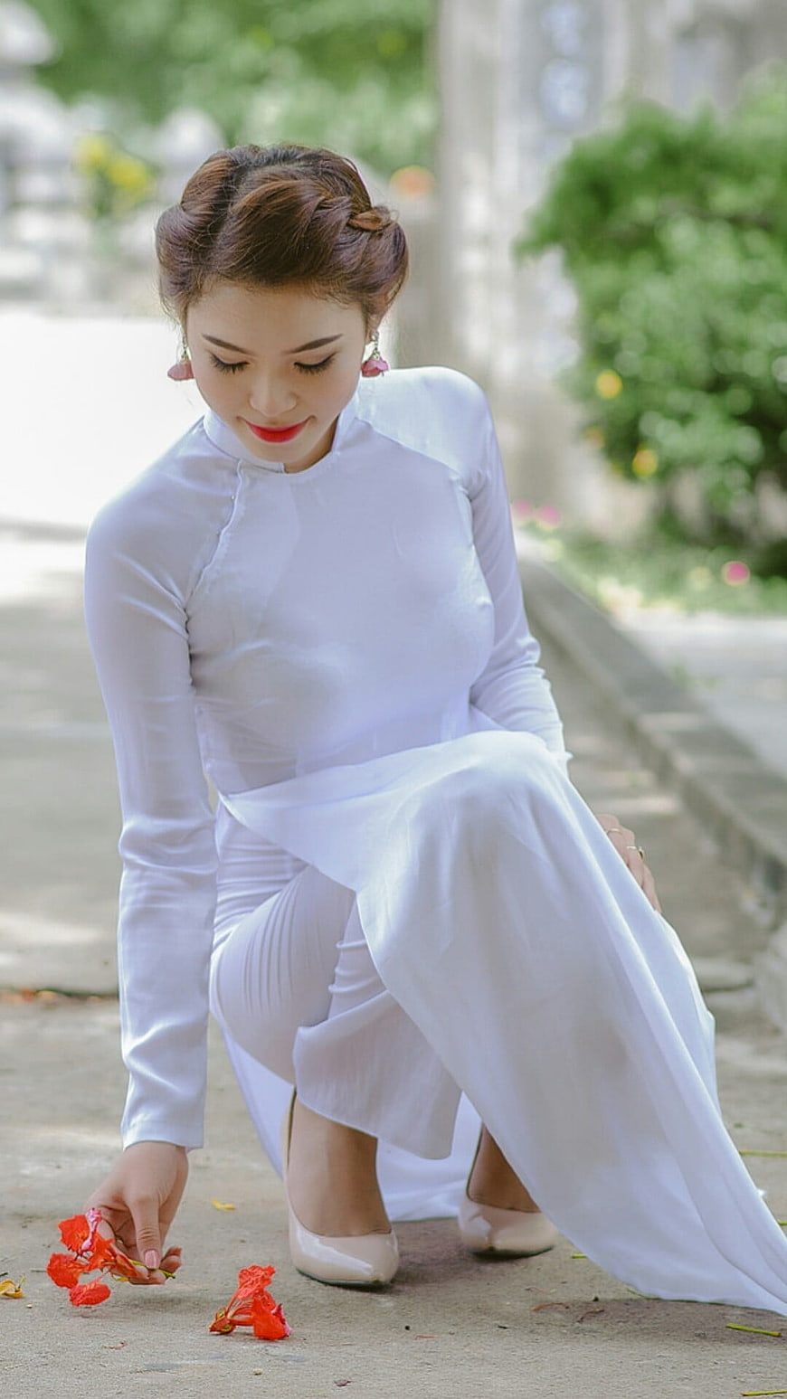 Vietnamese woman in white Ao Dai picking red flowers