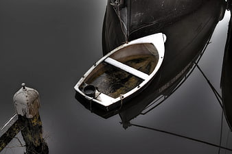 Small white dinghy tied to large black boat on calm water