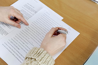 Hands Editing Manuscript with Pen on Wooden Desk