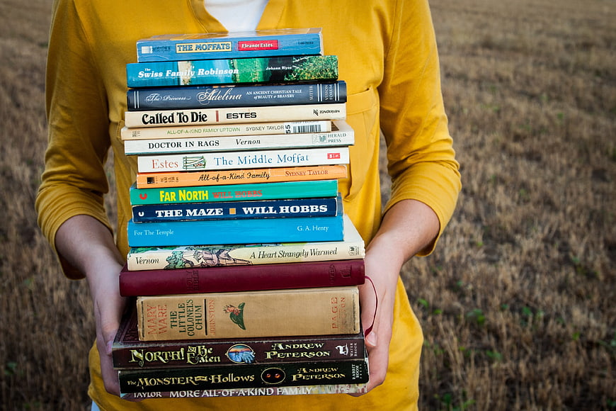 Person holding stack of classic books in field