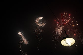 Fireworks exploding in night sky above street lamp