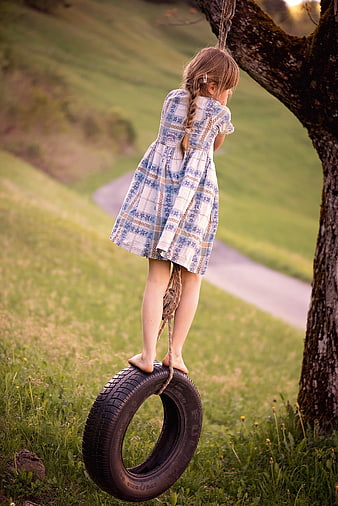 Little girl playing on a tire swing in a grassy field