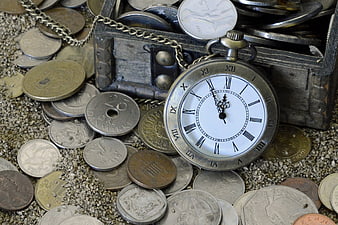 Antique pocket watch and coins on sand background