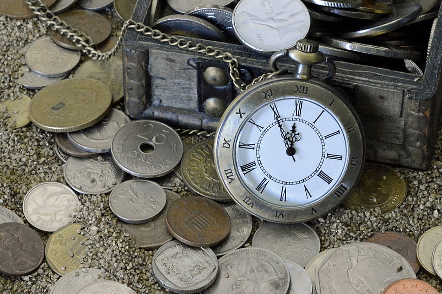 Antique pocket watch and coins on sand background