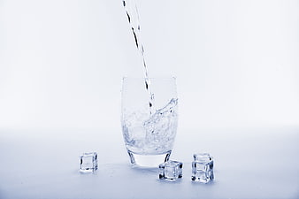 Water Pouring Into Glass With Ice Cubes On White Background