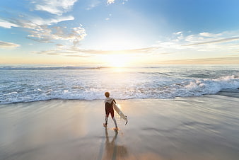 Surfer walking on beach at sunset with surfboard