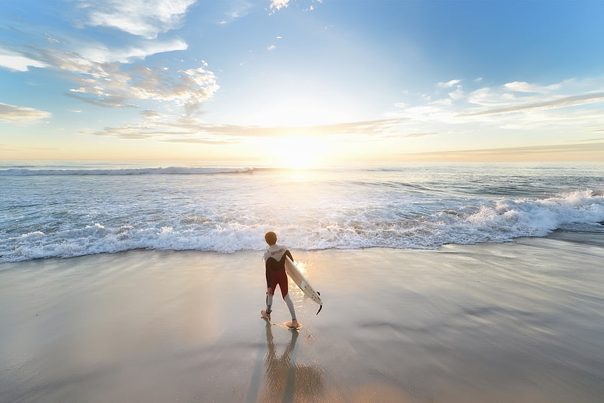 Surfer walking on beach at sunset with surfboard