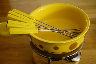 Yellow ceramic fondue pot with cheese-shaped forks on wooden table