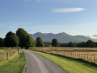 Rural country road leading to distant mountains under a clear blue sky