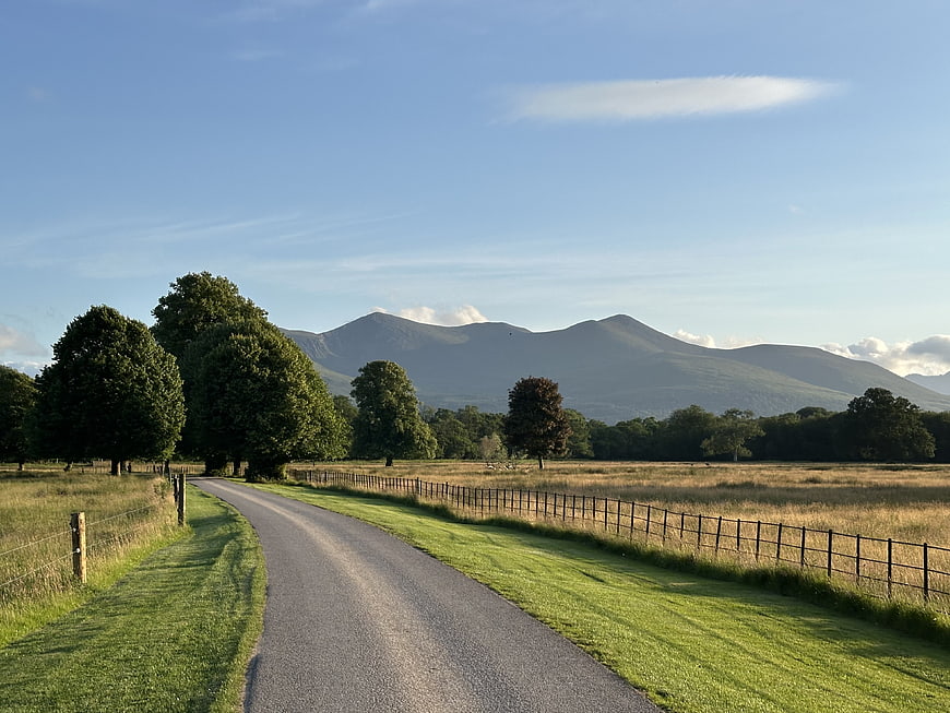 Rural country road leading to distant mountains under a clear blue sky
