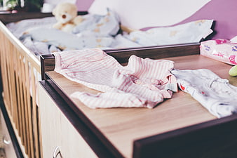 Baby clothes on changing table with crib in background