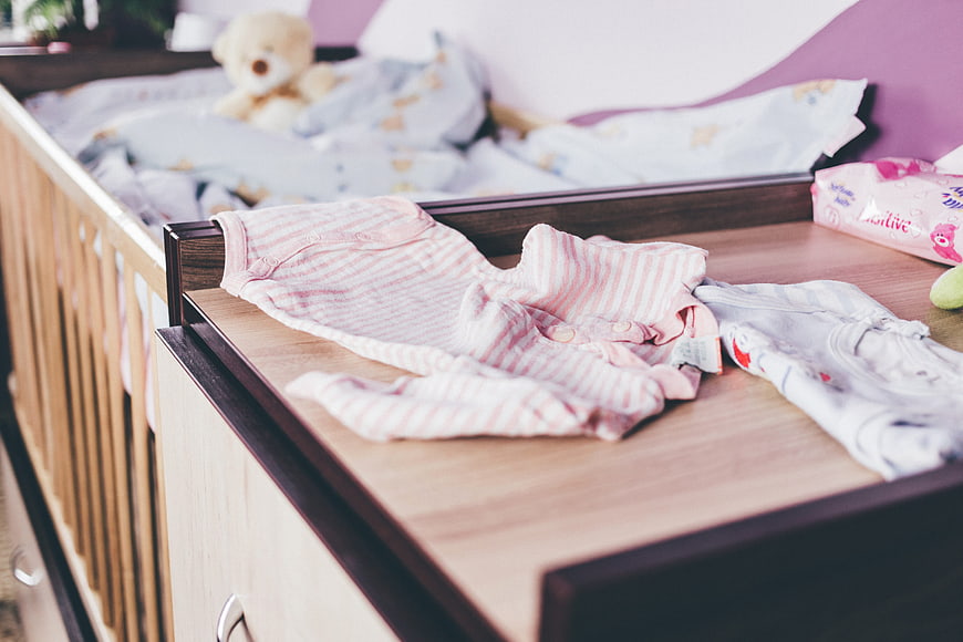 Baby clothes on changing table with crib in background