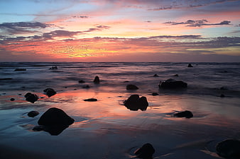 Serene Sunset Over Rocky Beach with Silhouetted Stones