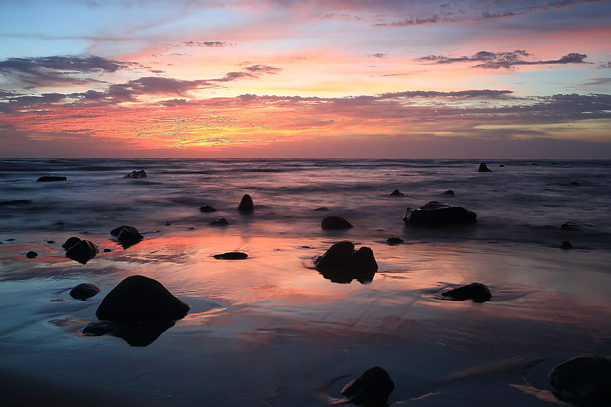 Serene Sunset Over Rocky Beach with Silhouetted Stones