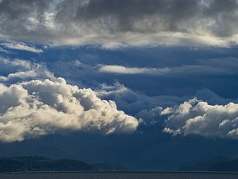 Dramatic Clouds Over Dark Ocean and Forested Hills