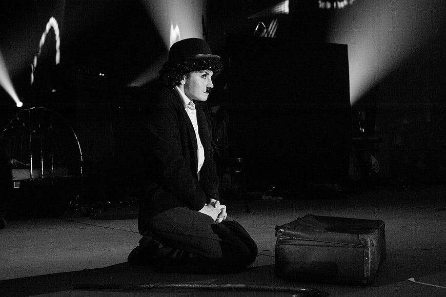 Charlie Chaplin Impersonator Kneeling on Stage with Suitcase