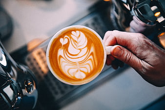 Barista Hand Holding Cup of Coffee with Intricate Latte Art