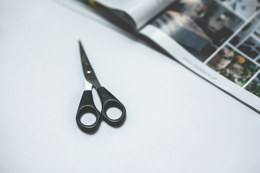 Black scissors on white paper with blurred magazine background