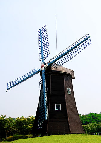 Traditional Brown Windmill with Blue Blades on Green Hill