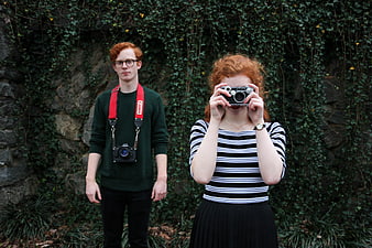 Red-haired couple with vintage cameras against ivy wall