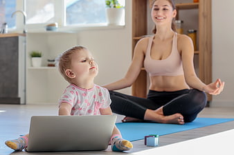 Mother doing yoga while toddler plays with laptop at home