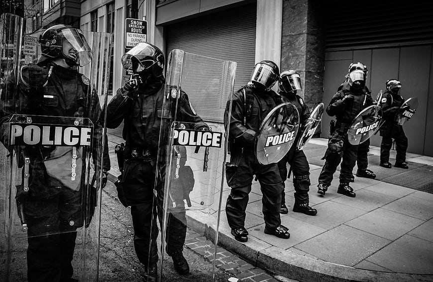 Black and white photo of riot police officers with shields on a city street