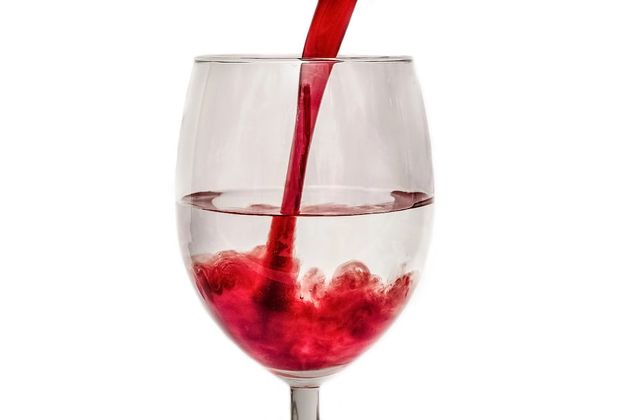 Red wine pouring into a clear glass on white background