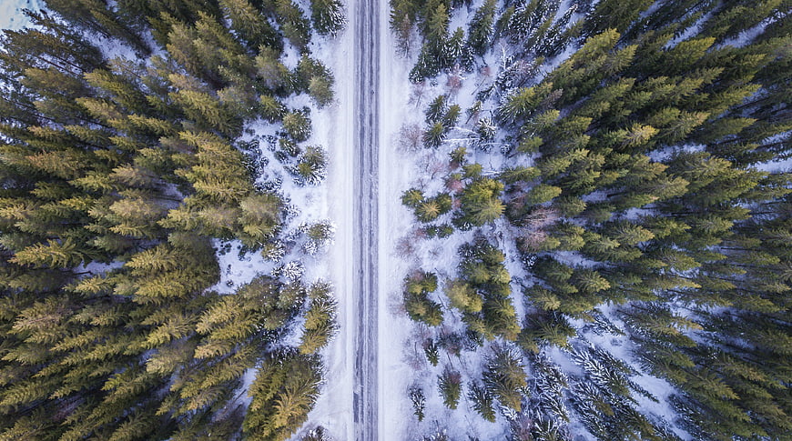 Aerial View of Snowy Road Through Winter Forest
