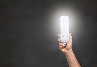 Hand holding glowing energy-saving light bulb against dark background
