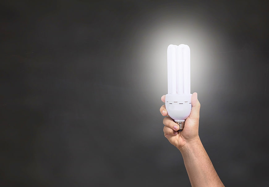 Hand holding glowing energy-saving light bulb against dark background