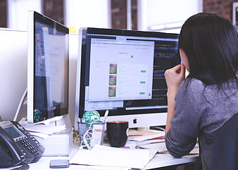 Woman working at dual monitor computer desk in office