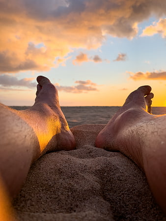 Bare feet on sandy beach at sunset with ocean horizon