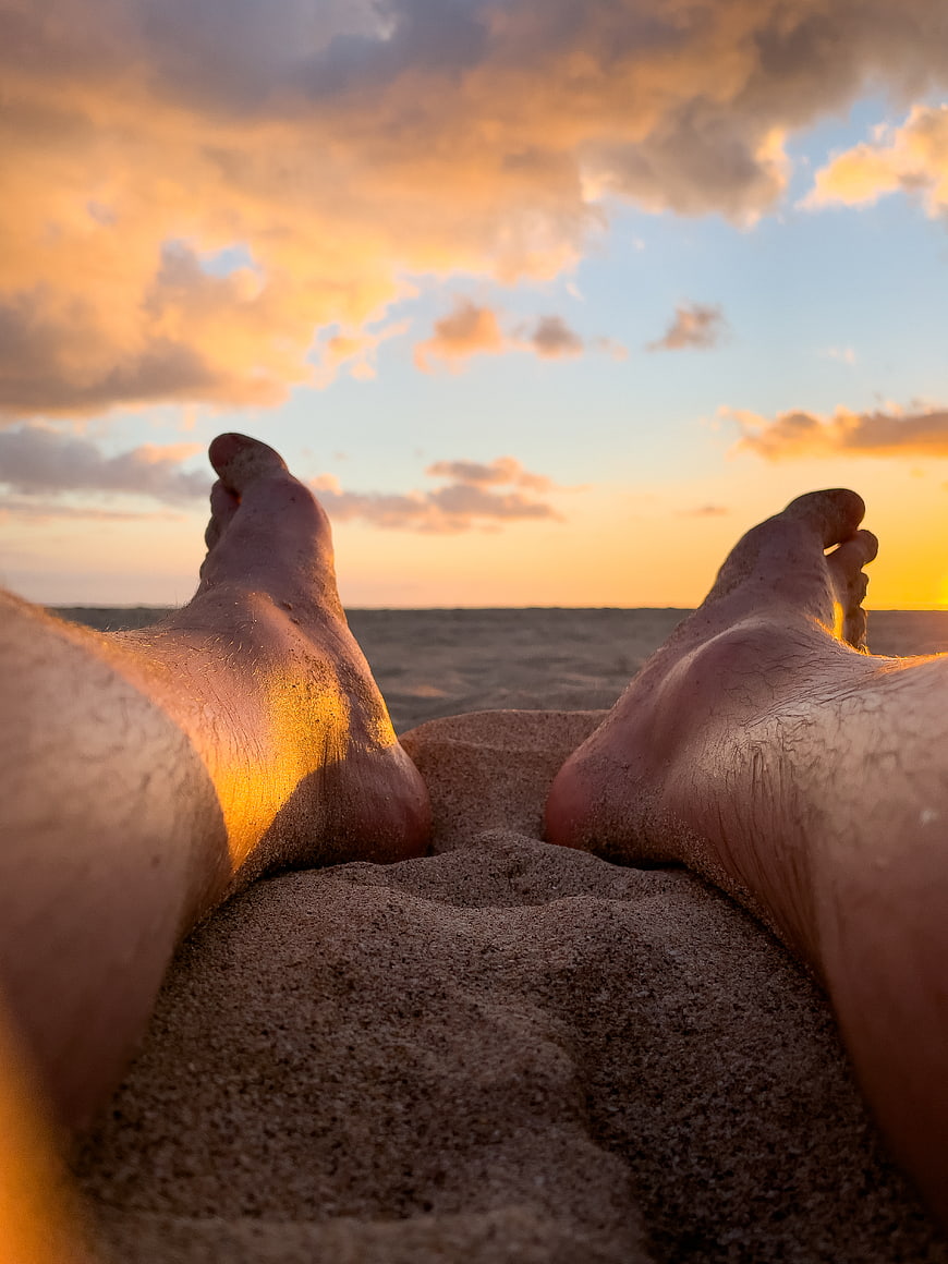 Bare feet on sandy beach at sunset with ocean horizon