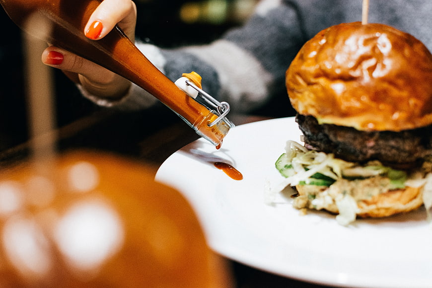 Close-up of hand pouring spicy sauce on gourmet burger