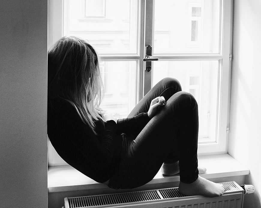 Sad woman sitting on window sill looking out