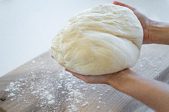 Hands holding fresh bread dough over floured wooden board