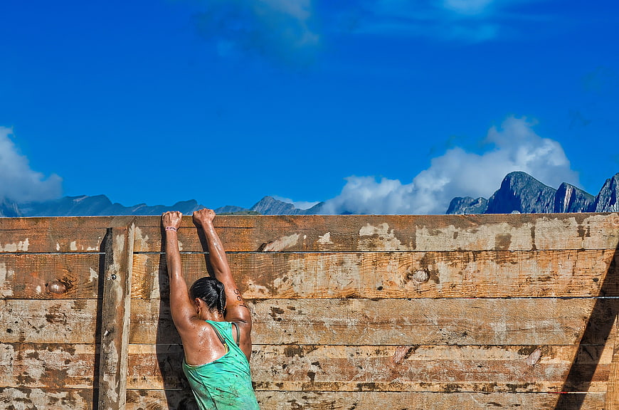 Woman climbing wooden obstacle wall in mountain obstacle course
