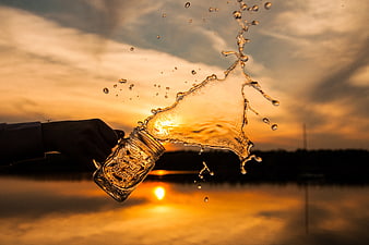 Hand holding mason jar with water splash at sunset
